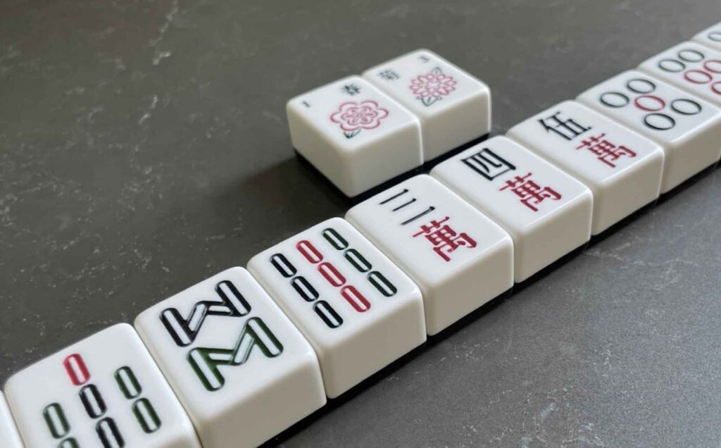 A sequence of Mahjong tiles arranged in a winning formation on a textured and dark surface.